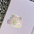 A vinyl die cut sticker with a metallic finish designed by Vikki Vinnie depicting a dragon resting on clouds