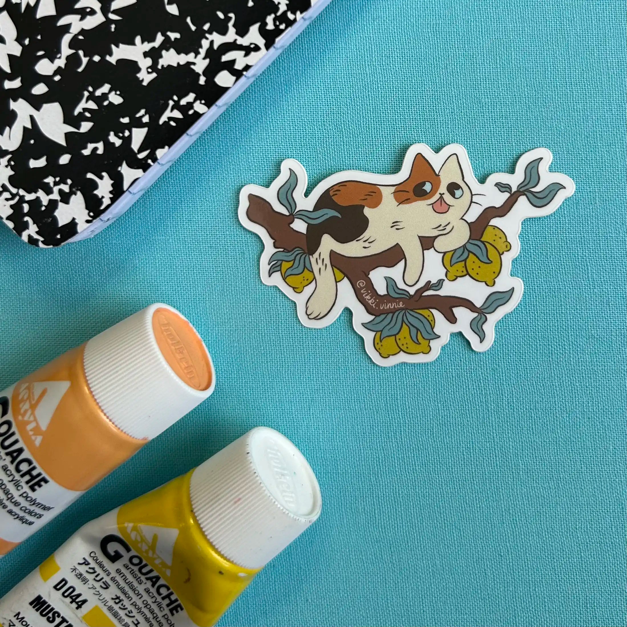 A die cut sticker designed by Vikki Vinnie depicting a calico cat sitting in a lemon tree