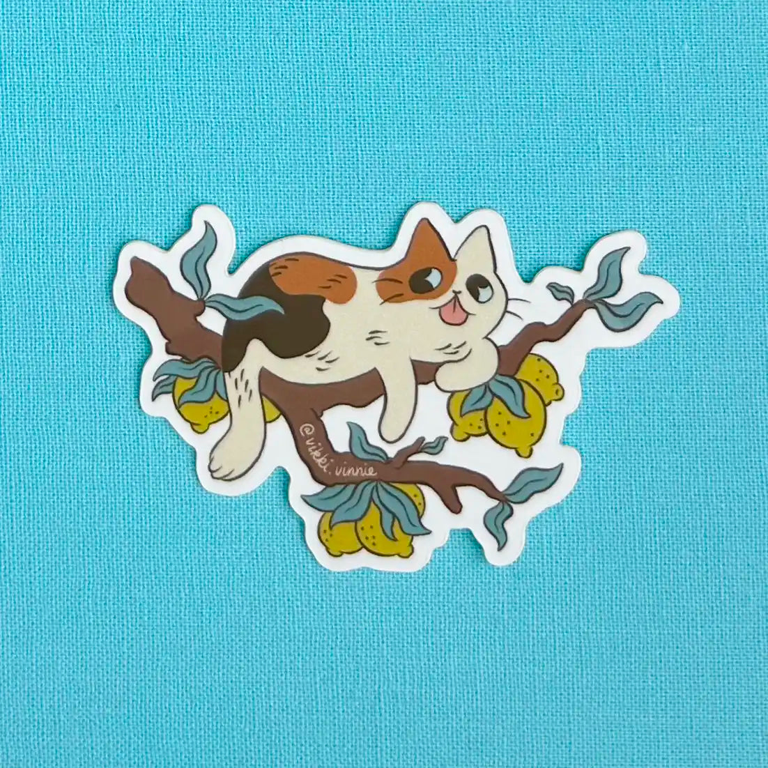 A die cut sticker designed by Vikki Vinnie depicting a calico cat sitting in a lemon tree