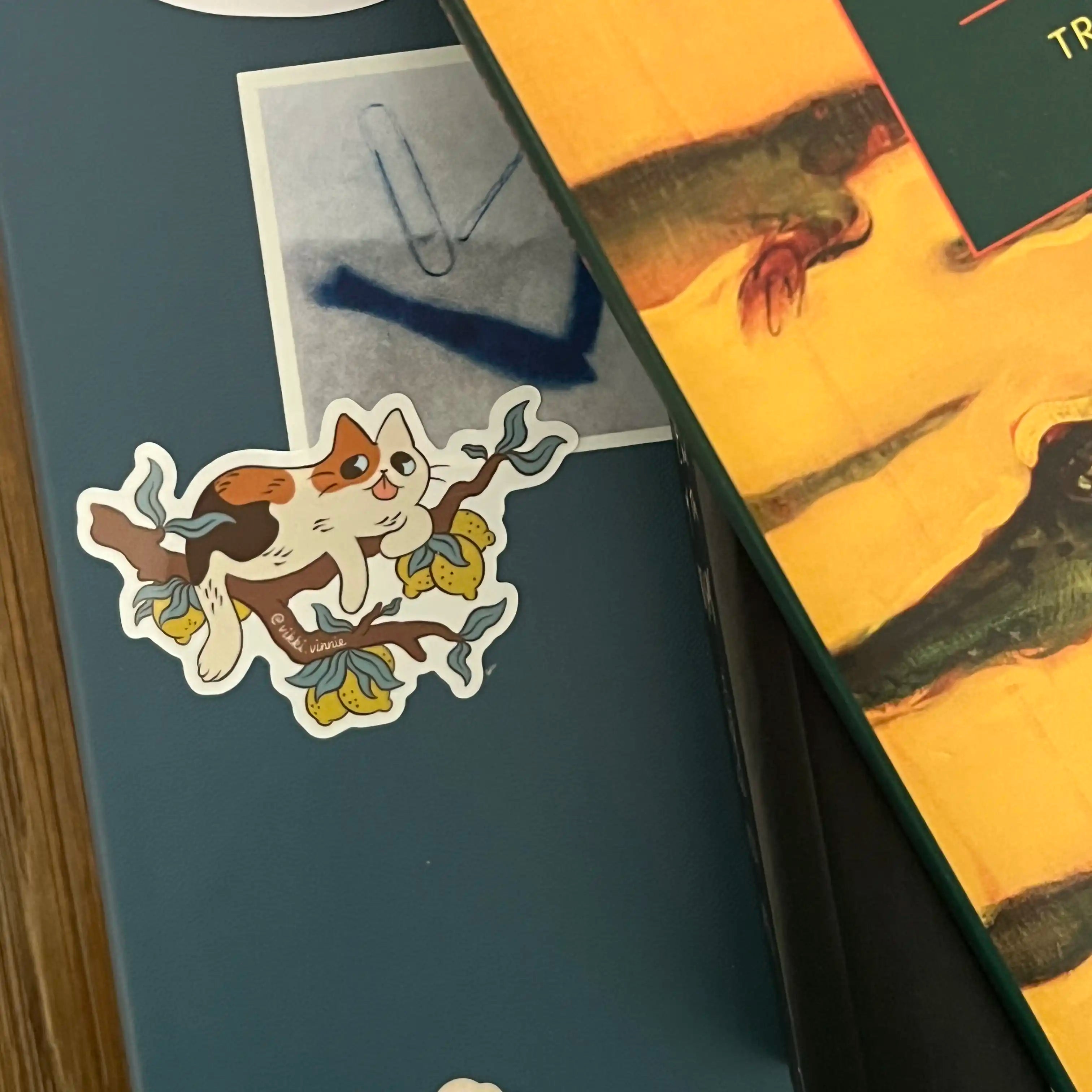 A die cut sticker designed by Vikki Vinnie depicting a calico cat sitting in a lemon tree