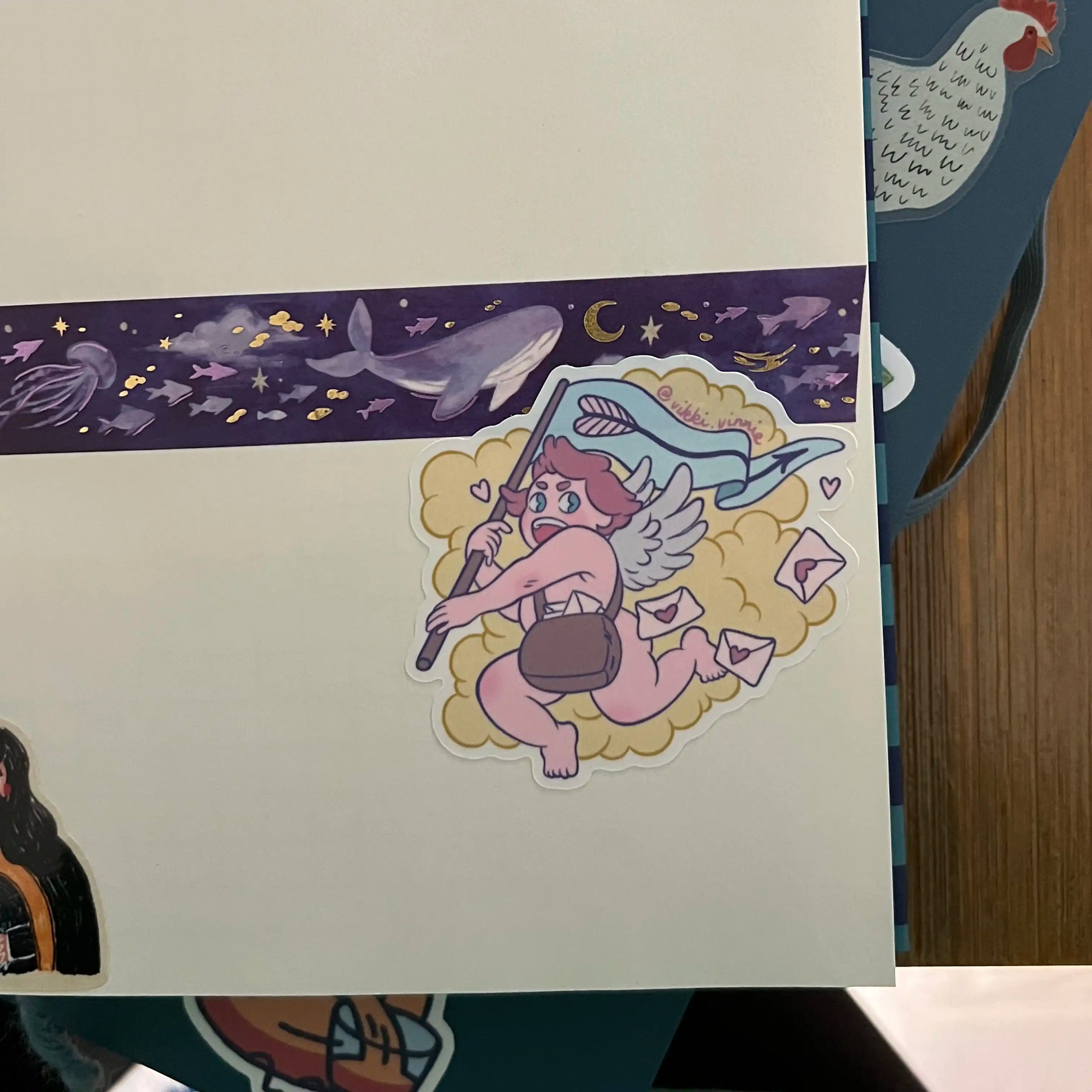 A vinyl die cut sticker designed by Vikki Vinnie depicting Cupid delivering Valentines